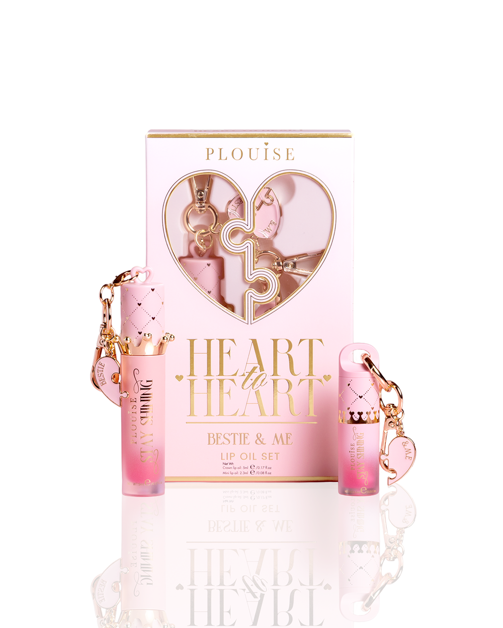 P.Louise Bestie & Me Heart To Heart Charm Lip Oil Set, featuring a pink and gold gift box with a heart-shaped window, flanked by two pink gradient lip oil tubes with diamond-patterned caps and keychain charms, on a white reflective surface.