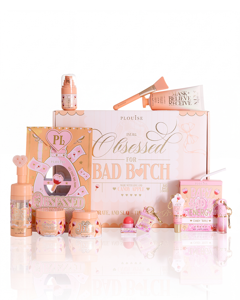 A P.Louise cosmetics gift set arranged on a white reflective surface, featuring a large pink and peach box, multiple cosmetic bottles, jars, and small packaged items in coordinated pastel pink and peach tones.