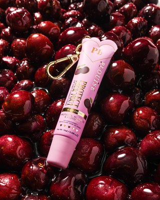 Pink black cherry scented tinted lip conditioner with gold clip on a bed of cherries