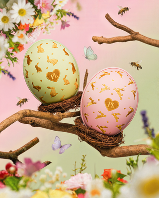 Two decorative pink and green Easter eggs with gold rabbit design on a branch with flowers and butterflies.