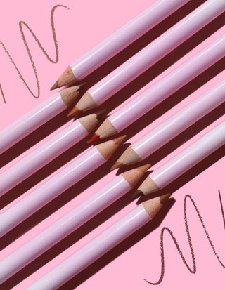 A collection of P.Louise sharpenable color lip liners in a pink hue, arranged parallel to each other against a pink background with swatch lines depicting the product's use.