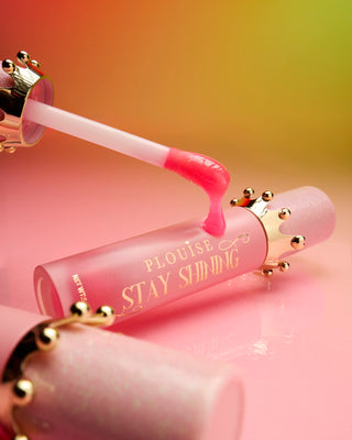 Pink tube of P.Louise STay SHining glossy lip oil laying on a pink surface with a lip oil wand resting against the tube showing the product