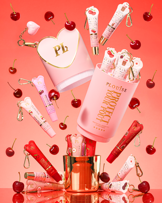Pink XL Protect Your Pout packaging that's opened surrounded by cherries and pink and red lip conditioners on a pinkbackground