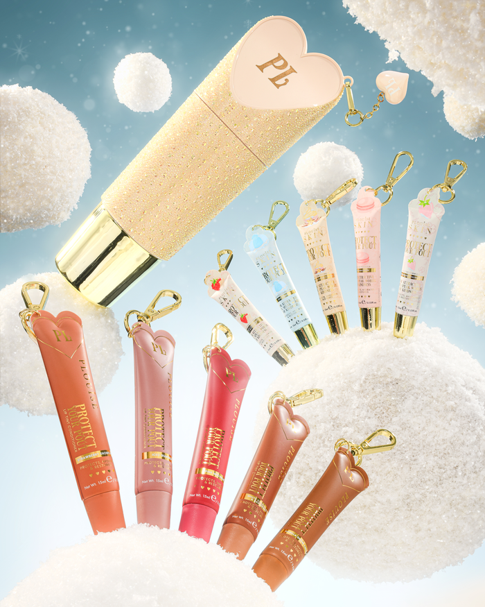 A set of heart-shaped lip conditioner keychain tubes with gold keychains, displayed against a whimsical background of fluffy white clouds and a light blue sky. The set includes a large gold glitter tube with a pink heart cap, and several various shades or regular sized lip conditioner tubes surrounding it.