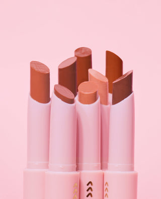 Close up on the tips of a set of P.Louise Glow Guide Glossy Lipstick Balm with various brown shade tips on a pink background