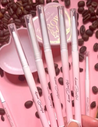 A collection of pink P.Louise eyebrow pencils with spoolie brushes on the end displayed on a pink surface with coffee beans scattered around.