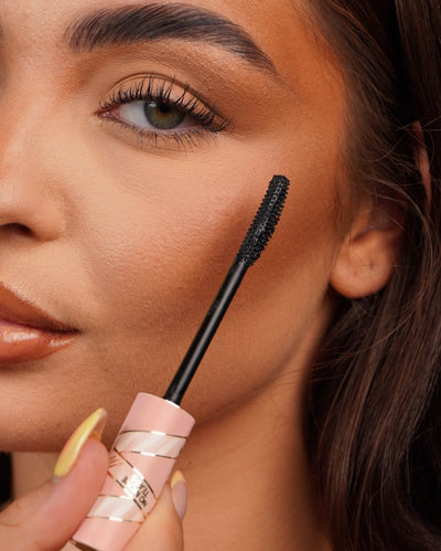 Close-up of the P.Louise Tearproof waterproof mascara wand held near a person's eye with a blurred background